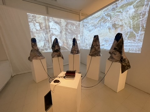 An image of the artwork Eye to Eye. Five shrouded, humanlike figures are placed in front of projected images.